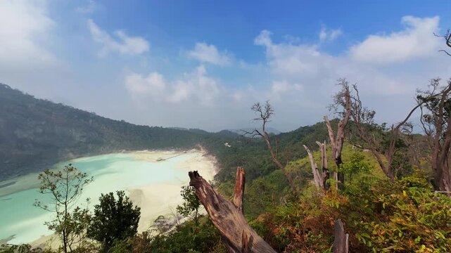 Wide-angle landscape timelapse video showing fast-moving white clouds over the turquoise volcanic crater lake of Kawah Putih, captured from Sunan Ibu viewpoint in Ciwidey, Bandung, Indonesia