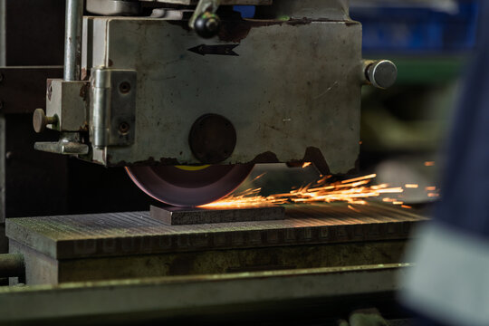 Grinding wheel cuts across metal surface and throws bright spark trail, revealing active machining process and precision finishing task inside industrial workshop during heavy equipment operation.