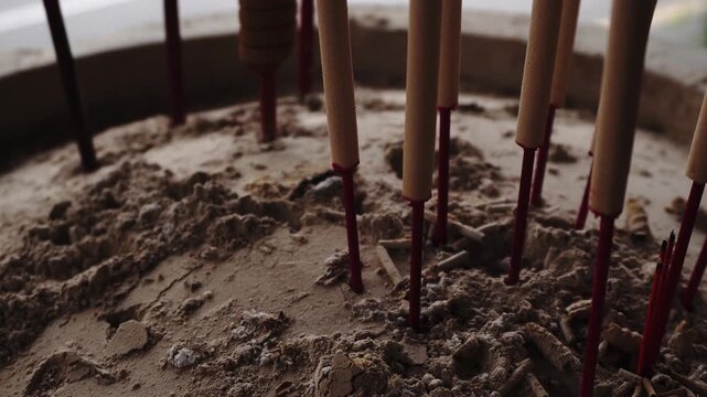 Close-up of incense sticks standing upright in a sand-filled urn, some unlit