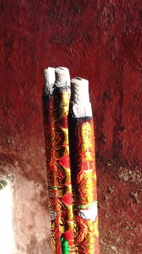 Close-up of burning incense sticks with embossed red and gold patterns against a textured red wall