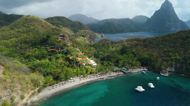Aerial parallax reveals hillside resort villas overlooking curved beach and turquoise bay with Pitons peaks in Saint Lucia