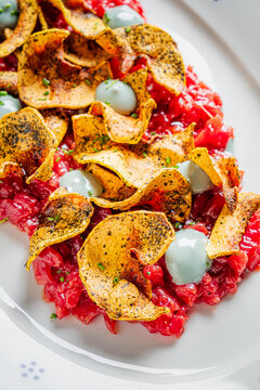 Crispy potato chips atop vibrant tomato tartare for a delightful culinary experience