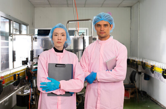 Portrait of two young workers standing with clipboard and laptop in factory, quality control officer in beverage production line factory.