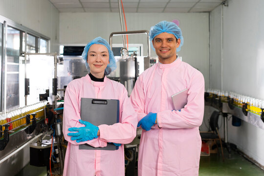 Portrait of two young workers standing with clipboard and laptop in factory, quality control officer in beverage production line factory.