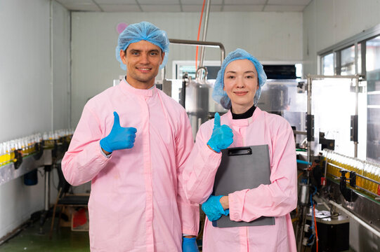 Portrait of two young workers standing with clipboard and laptop in factory, quality control officer in beverage production line factory.