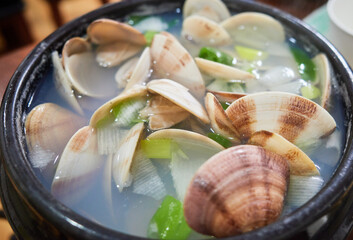 Steaming clear silk clam soup in a traditional black earthen bowl with green scallions. This refreshing South Korean seafood broth is widely enjoyed as a hangover remedy and authentic dining delicacy. © 진영김