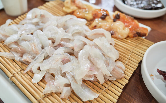 Fresh translucent filefish sashimi elegantly served on a traditional bamboo mat accompanied by vibrant sea squirt This authentic South Korean seafood delicacy highlights premium dining and gastronomy