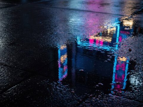 Neon reflections rain puddle night city wet pavement glow creates cinematic moody atmosphere under blurred colorful lights and glossy surface