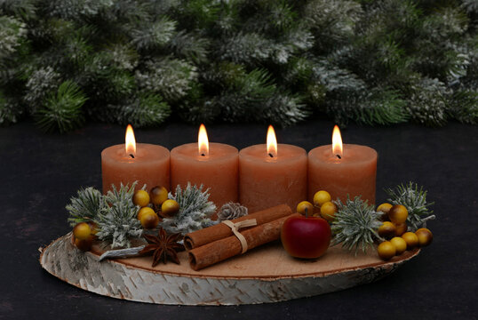 Rustic Advent arrangement with four candles on a wooden tray; four candles are burning for the fourth Sunday of Advent.