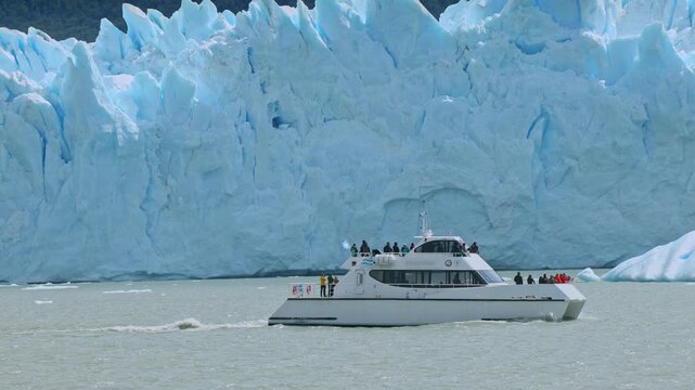 Tour boat excursion moving past massive blue walls of Perito Moreno Glacier in Patagonia Argentina