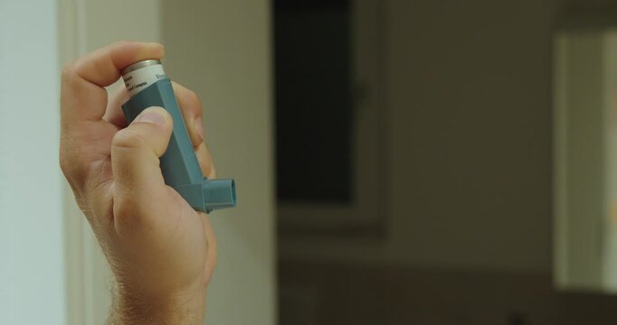 Close-up of a hand spraying an asthma inhaler.