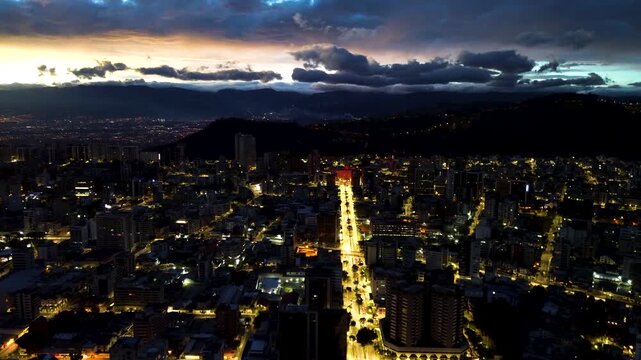 Dusk Drone View of Quito Ecuador Avenue with City Lights, Mountain Silhouette, Urban Buildings and Dramatic Evening Sky