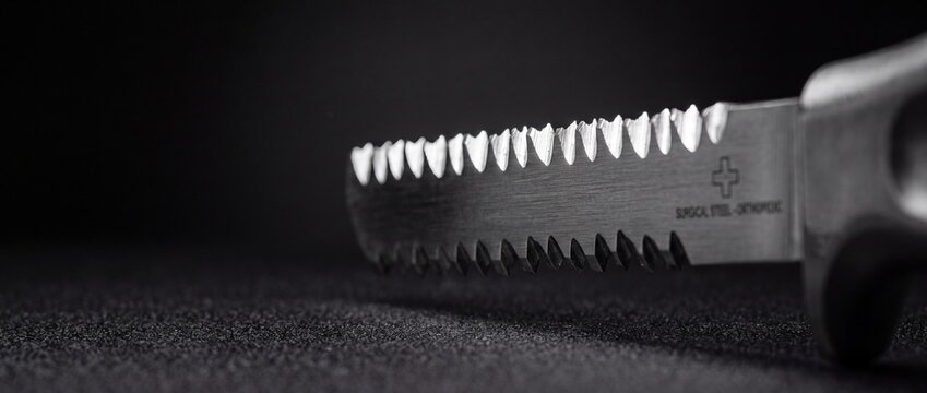 Surgical steel orthopedic saw blade with sharp teeth on dark background.