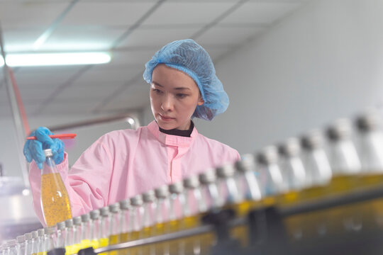 Young beautiful  white woman inspector standing in front of assembly line with capped bottled drinks and examining plastic packaging.