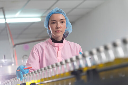 Young beautiful  white woman inspector standing in front of assembly line with capped bottled drinks and examining plastic packaging.