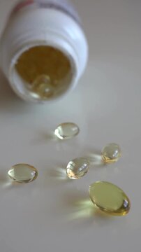 Fish oil omega 3 supplements spilling out of a packer bottle on a white background.