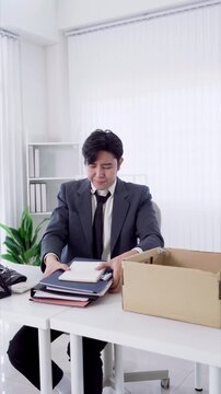 Young Asian businessman packing personal items into cardboard box after resignation in bright office