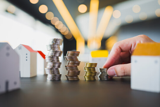 Real estate and property investment concept with hand stacking coins beside miniature house models on table for housing savings, mortgage home loan down payment and financial growth.