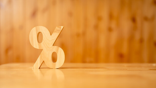 Interest rate and discount percentage concept with wooden percent symbol on table against warm wooden wall background with copy space for financial loan, banking credit and tax calculation.