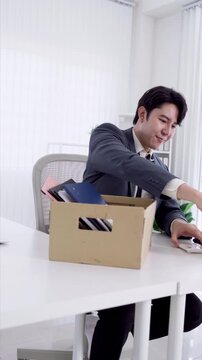 Young Asian businessman packing personal belongings into box while resigning from office job