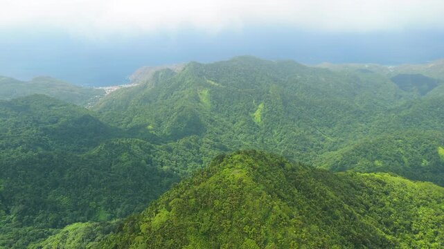 Aerial parallax shot glides over misty forested mountains revealing distant Piton peaks and coastline in Saint Lucia