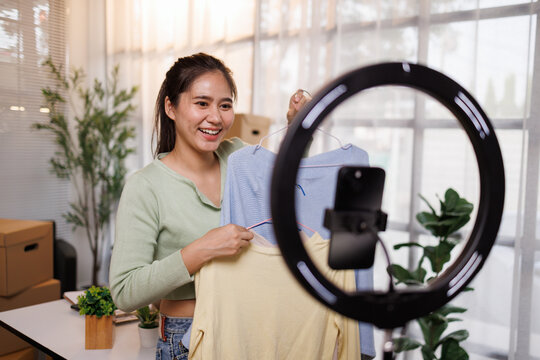 Young woman creating content and live streaming her online clothing sales with a smartphone and ring light for e commerce and social media marketing