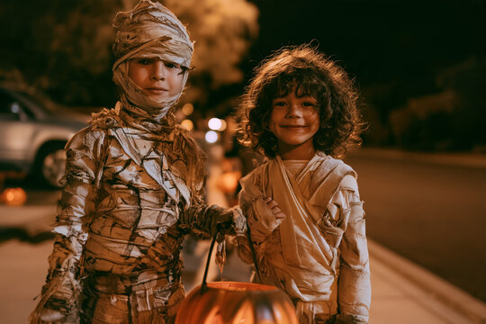 Mummy on Halloween Night Two Children in Wrapped Costumes Trick or Treating Together on a Neighborhood Street