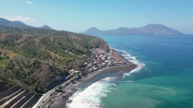 Aerial view of scenic coastal road and black sand beach with turquoise sea in Ende, East Nusa Tenggara, Indonesia.
