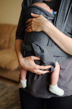 Mother with ergo baby carrying toddler at home in sling. While baby is sleeping