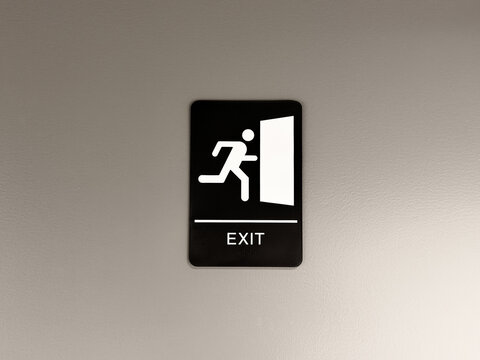 ADA compliant black exit sign with running figure and door on gray wall