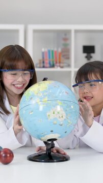 Two Young School Girls in Lab Coats Examining a World Globe