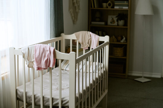 Empty wooden baby crib standing in nursery room near window. Concept of infant care, maternity preparation and parenting, suitable for nursery furniture advertising