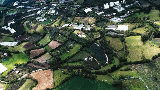 Top Down Drone View of Patchwork Agricultural Fields in Ecuador Mountain Valley, Greenhouses, Rural Roads and Andean Countryside