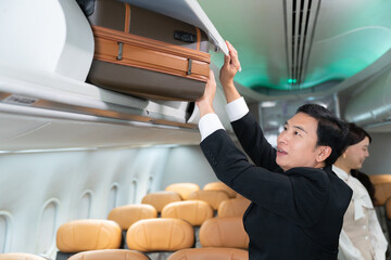Male flight attendant storing passenger luggage in overhead compartment © DG PhotoStock