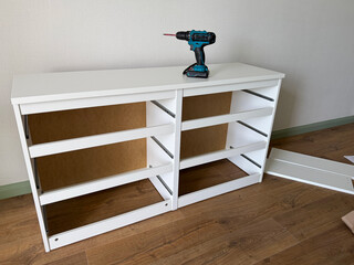 DIY furniture assembly in a modern apartment. White cabinet being assembled with a cordless drill during home renovation and interior furnishing © leroy
