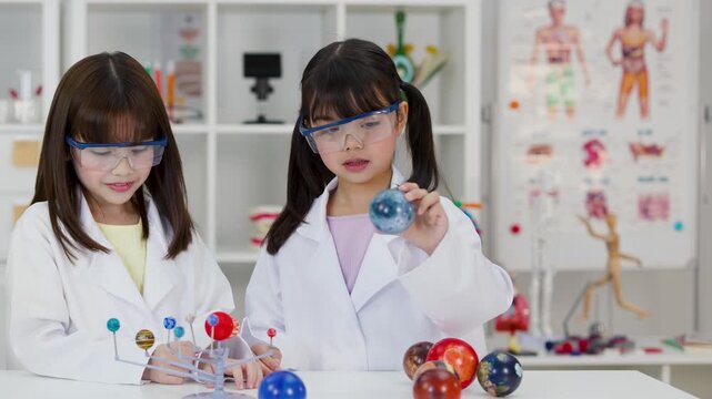 Two Young Schoolgirls Studying Solar System Model in Science Lab