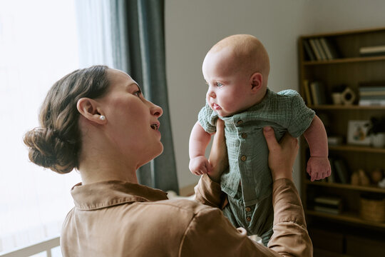 Caucasian mother holding baby up during bonding time at home, representing maternity care and early childhood development. Useful for pediatric healthcare and parenting campaign
