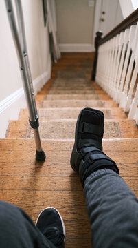 Person with injured leg in orthopedic boot walking down stairs with crutch
