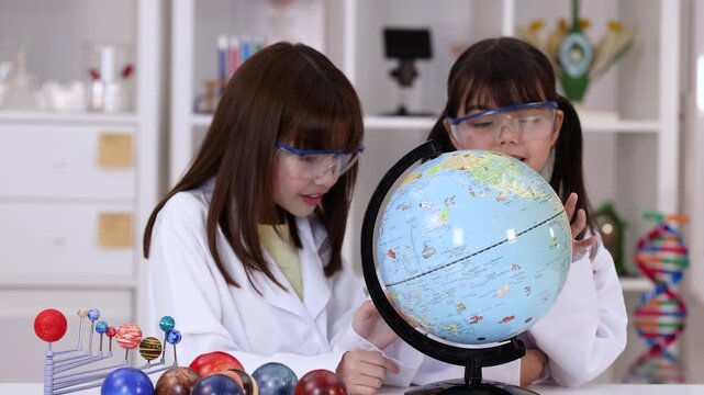 Two Young Girls in Lab Coats Studying a World Globe