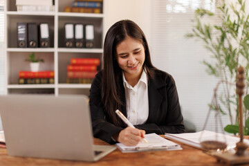 Young legal professional working in law office, reviewing documents and making notes, using laptop...