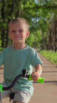 Smiling little boy riding a bicycle in a sunny neighborhood for the first time. Young happy child learning to ride a bike on a summer day. Close up of a joyful kid riding a bicycle in slow motion.