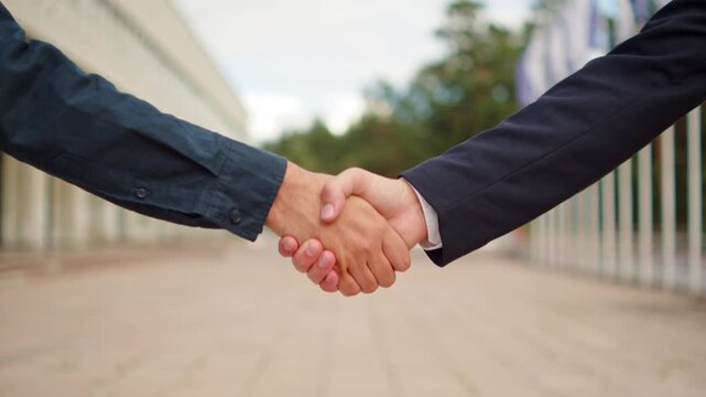 Two business partners shaking hands outdoors. Firm handshake between two professionals in corporate suits.