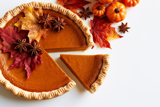 Sliced pumpkin pie with autumn leaves, star anise and mini pumpkins, Thanksgiving flat lay
