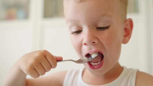 Little boy sitting at a table and eating hot porridge for breakfast at home. Adorable toddler boy enjoying a healthy morning meal. Kid eating organic porridge with a spoon at his small kids table.