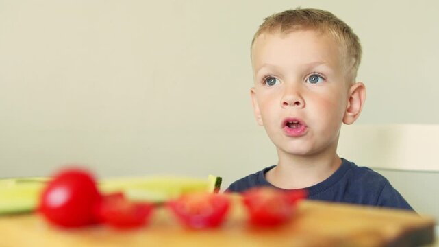 A close‑up of a four years old boy eating fresh vegetables: cucumbers and tomatoes. The concept of healthy eating