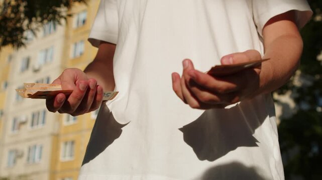 Person counting a small amount of paper money and showing disappointment. Close-up of hands holding a few cash bills with an empty gesture showing a lack of money. 