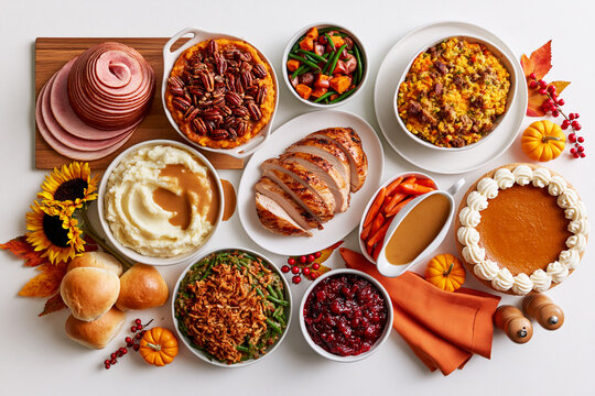 Thanksgiving dinner spread overhead with sliced ham, turkey, mashed potatoes, pumpkin pie and sides