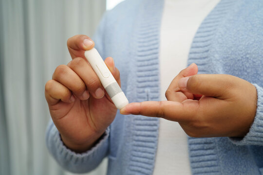 Asian woman self testing to check blood sugar level diabetes by digital lancet on finger at home.