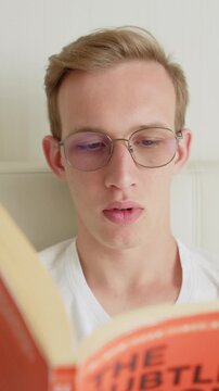 Portrait of a young man with glasses reading a book at home.