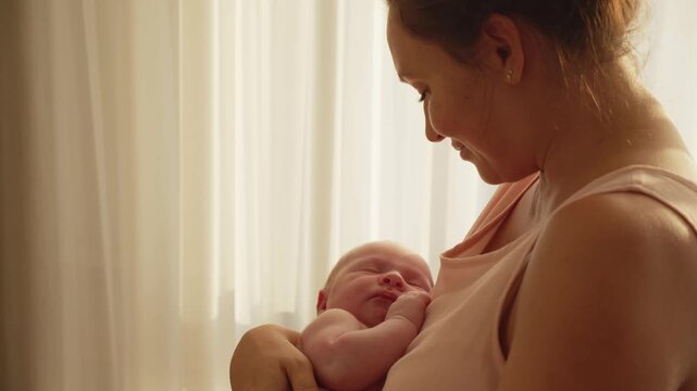 Happy mother holds a baby in her arms at sunset. A cute infant sleeps in his mother's arms. Concept of happy parenthood. Mother is rocking her newborn son in her arms. Mother and child.